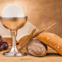 Kielich z hostią, winogrona, chleb i kłosy zbóż – symbole Eucharystii na drewnianym stole.