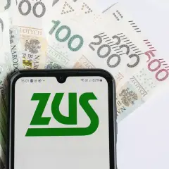 Telefon z logo ZUS na tle polskich banknotów. Może to symbolizować zwrot składki zdrowotnej lub inne rozliczenia z ZUS.
