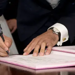 Mężczyzna w garniturze składa parafkę na dokumencie. Elegancki zegarek i spinki do mankietów podkreślają uroczystość chwili.