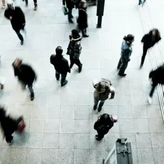 Ludzie w ruchu, ich sylwetki rozmyte przez fluktuację, tworzą dynamiczny obraz miejskiego zgiełku.