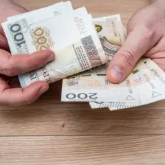 Dłonie trzymające polskie banknoty: 100 i 200 złotych. Widać fragment zegarka na ręce.