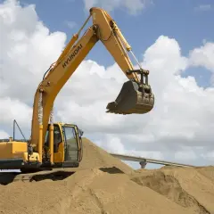 Żółta koparka Hyundai na budowie, operator koparki przygotowuje się do pracy na stercie piasku.