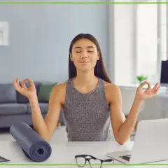 Kobieta medytuje przy biurku, osiągając work life balance. Obok leży mata do jogi i laptop.