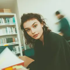 Młoda kobieta w okularach, otoczona książkami, studiuje w bibliotece. Ibiden, nauka i wiedza.