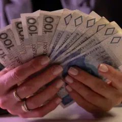 Dłonie trzymające plik banknotów 100 zł i 50 zł. Taki jest koszt życia.