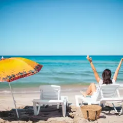 Kobieta cieszy się słońcem na plaży, zastanawiając się, ile dni urlopu jeszcze jej zostało. Obok parasol i leżaki.