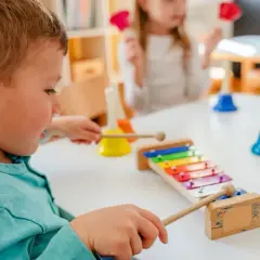 Chłopiec aktywnie w żłobku gra na cymbałkach, obok inne dzieci bawią się dzwonkami.