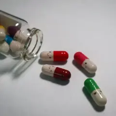 Kapsułki psychotropowe z uśmiechniętymi buźkami, jedna buteleczka przewrócona, leżą na białym tle.