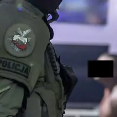 Funkcjonariusz CBŚ w kamizelce z napisem POLICJA i godłem Polski. W tle mężczyzna z zamaskowaną twarzą.
