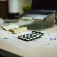 Kalkulator na biurku obok laptopa i notatnika. Czy to już czas na podsumowanie, co netto?