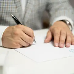 Mężczyzna w eleganckim garniturze podpisuje dokument, ustalając wielkość nabywanego udziału w rzeczy lub w prawie majątkowym.