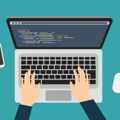Programista pisze kod na laptopie, obok leży smartfon i myszka.