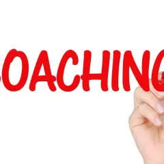 Ręka pisze czerwonym markerem słowo "COACHING". To proces rozwoju, który może obejmować lingwistykę.