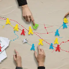 Ręce kierują kolorowymi ludzikami, tworząc ścieżki. To metafora **socjalizacji** i budowania relacji w grupie.