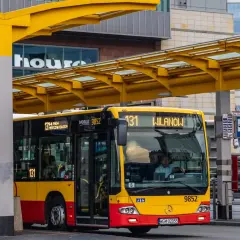 Żółto-czerwony autobus miejski na przystanku. Kierowca autobusu, jak i pasażerowie, zastanawiają się, ile zarabia kierowca autobusu.