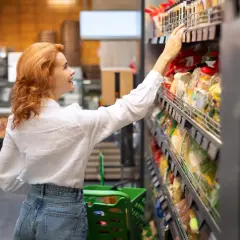 Kobieta z rudymi włosami wybiera produkty FMCG (towary szybko zbywalne) w supermarkecie.