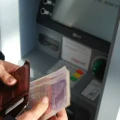 Ręce trzymają portfel i banknoty przy bankomacie. Czyżby czekał go deficyt?