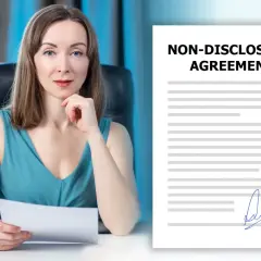 Kobieta z dokumentem w ręku obok umowy o poufności (NDA). Co to jest NDA? To umowa o zachowaniu poufności.