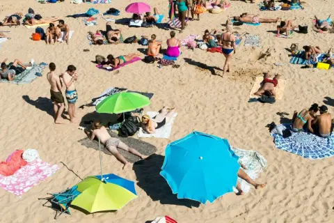 Wakacje pod gruszą na plaży. Ludzie opalają się, odpoczywają pod parasolami, ciesząc się słońcem i piaskiem.