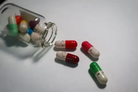 Kapsułki psychotropowe z uśmiechniętymi buźkami, jedna buteleczka przewrócona, leżą na białym tle.