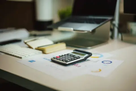 Kalkulator na biurku obok laptopa i notatnika. Czy to już czas na podsumowanie, co netto?