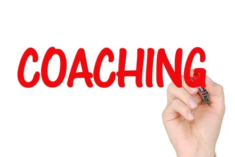 Ręka pisze czerwonym markerem słowo "COACHING". To proces rozwoju, który może obejmować lingwistykę.