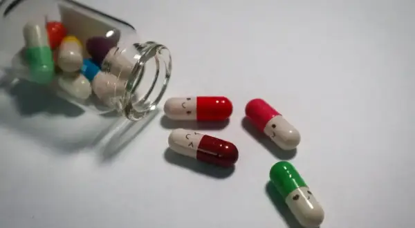 Kapsułki psychotropowe z uśmiechniętymi buźkami, jedna buteleczka przewrócona, leżą na białym tle.