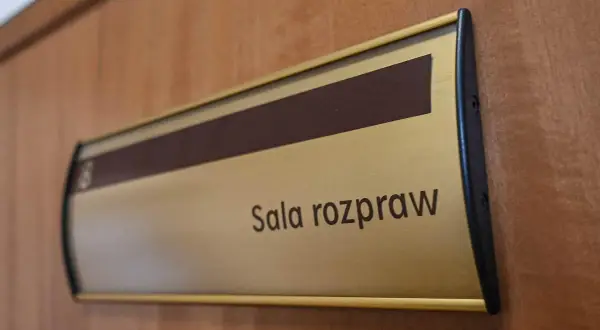 Tabliczka "Sala rozpraw" na drewnianych drzwiach. Może tu pracować referendarz sądowy.