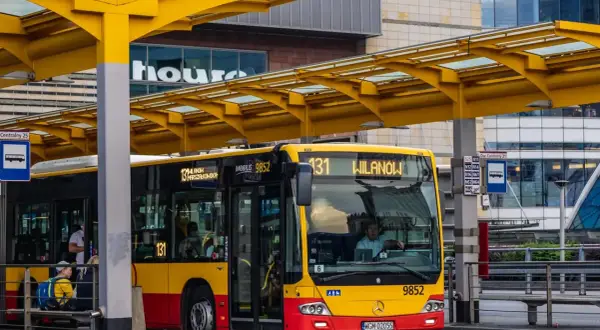 Żółto-czerwony autobus miejski na przystanku. Kierowca autobusu, jak i pasażerowie, zastanawiają się, ile zarabia kierowca autobusu.