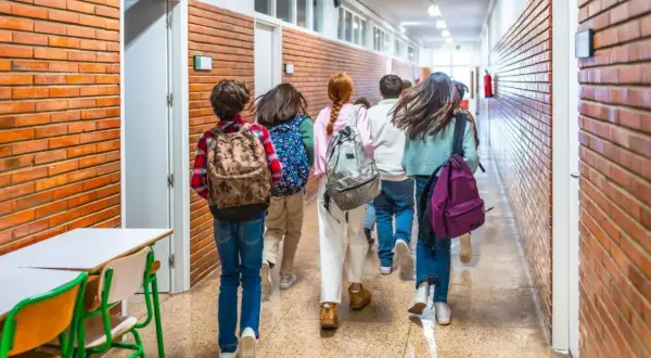 Dzieci z plecakami idą szkolnym korytarzem. Wszyscy mają równe szanse na edukację, to ważny parytet.