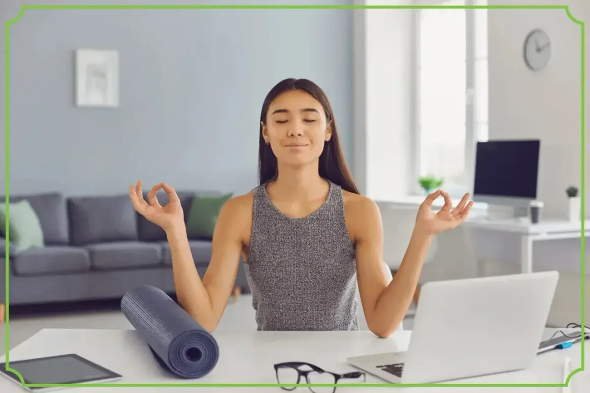 Kobieta medytuje przy biurku, osiągając work life balance. Obok leży mata do jogi i laptop.