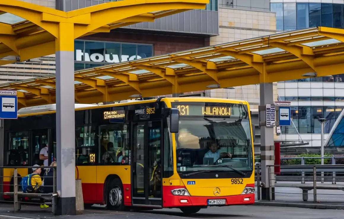 Żółto-czerwony autobus miejski na przystanku. Kierowca autobusu, jak i pasażerowie, zastanawiają się, ile zarabia kierowca autobusu.