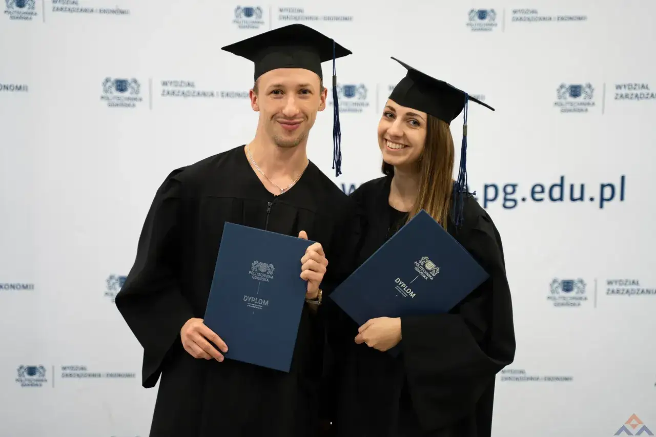 Uśmiechnięci absolwenci w togach z dyplomami, świętujący zakończenie studiów podyplomowych.