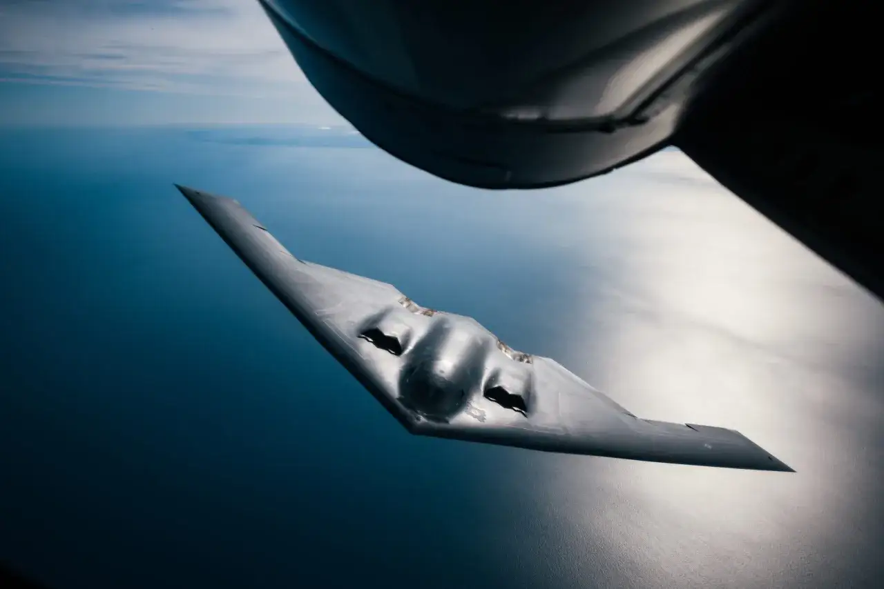 Niezwykły samolot bombowy B-2 Spirit leci nad oceanem, jego futurystyczny kształt odbija się w wodzie.
