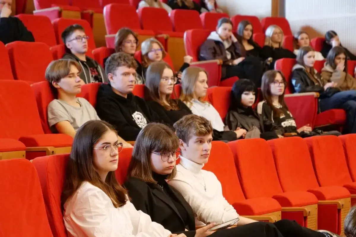Grupa studentów na wykładzie z psychologii, siedzą w czerwonych fotelach, uważnie słuchając.