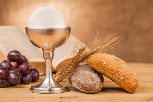 Kielich z hostią, winogrona, chleb i kłosy zbóż – symbole Eucharystii na drewnianym stole.