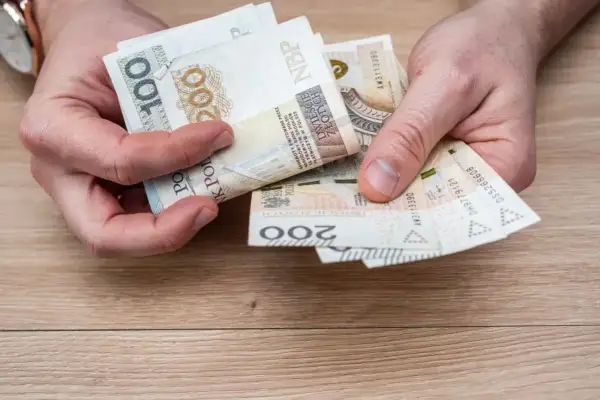 Dłonie trzymające polskie banknoty: 100 i 200 złotych. Widać fragment zegarka na ręce.