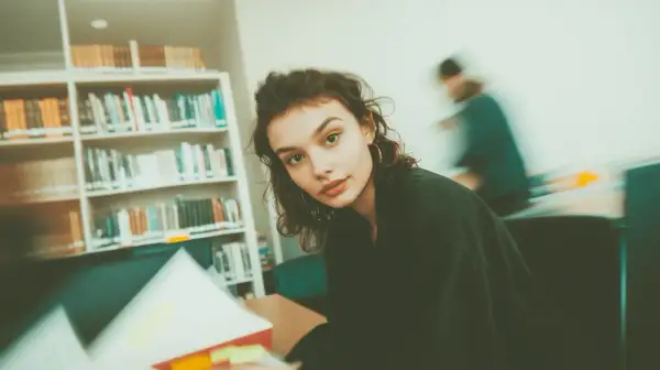 Młoda kobieta w okularach, otoczona książkami, studiuje w bibliotece. Ibiden, nauka i wiedza.