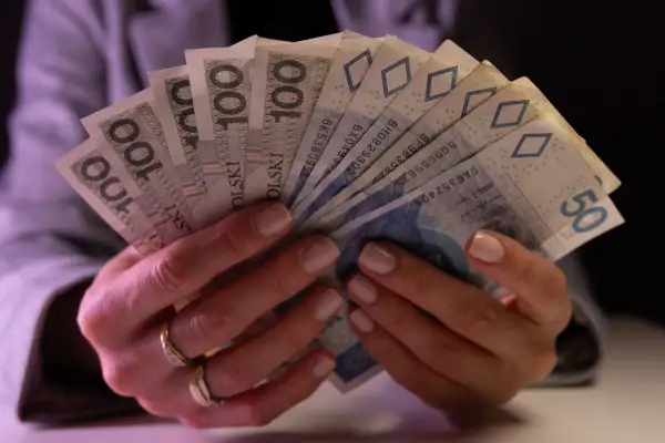 Dłonie trzymające plik banknotów 100 zł i 50 zł. Taki jest koszt życia.