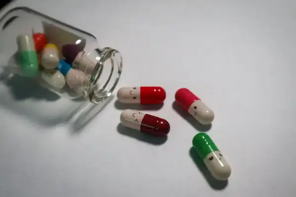Kapsułki psychotropowe z uśmiechniętymi buźkami, jedna buteleczka przewrócona, leżą na białym tle.