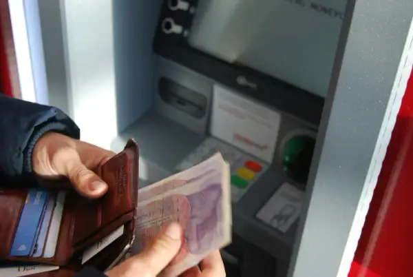 Ręce trzymają portfel i banknoty przy bankomacie. Czyżby czekał go deficyt?