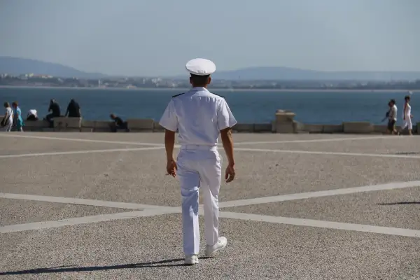 Młody marynarz w białym mundurze idzie w stronę morza.